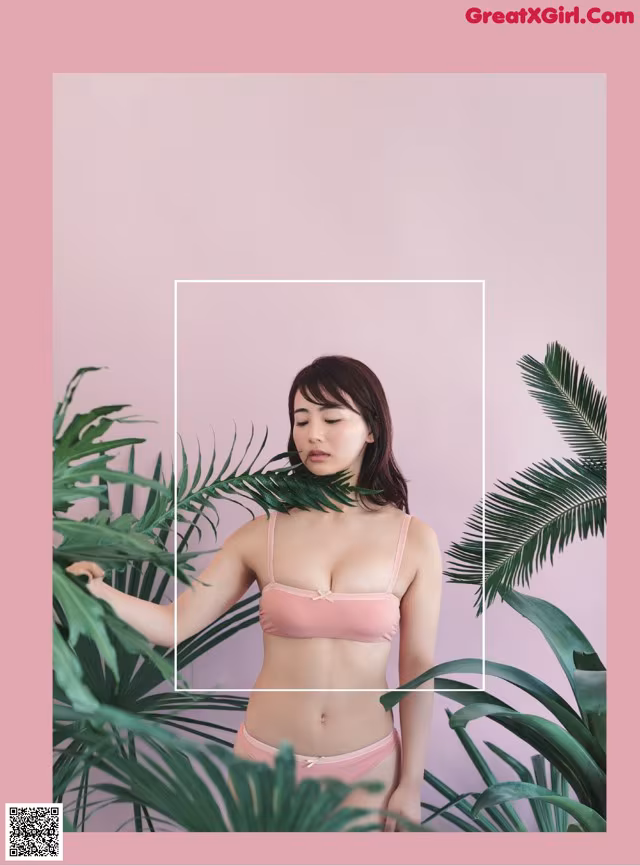 A woman in a pink bikini standing in front of a plant.