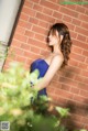 A woman in a blue dress leaning against a brick wall.