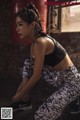A woman in a black sports bra top and patterned leggings crouching on the ground.