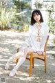 A woman sitting on a wooden chair in a white dress.