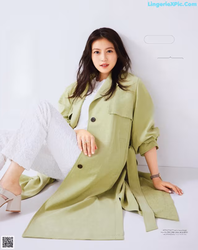 A woman in a green coat sitting on a white surface.