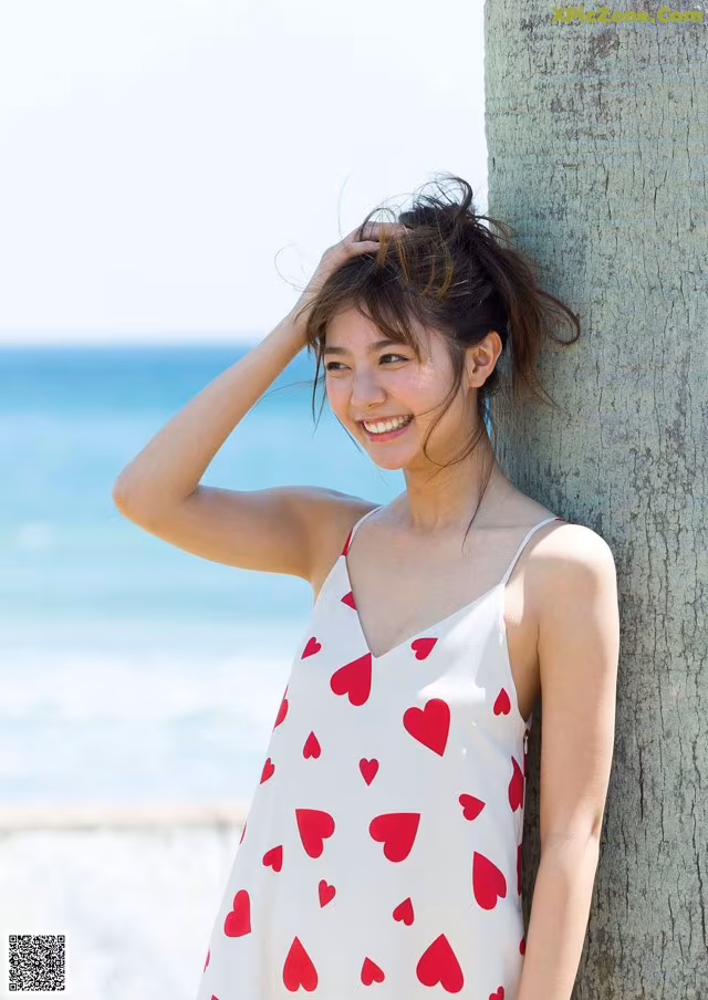 A woman leaning against a palm tree on the beach.