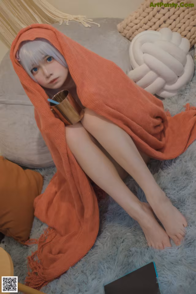 A woman sitting on a bed wrapped in a blanket.