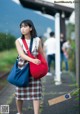 A woman in a plaid dress carrying a red bag.