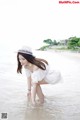 A woman in a white dress and hat standing in the water.