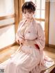 A woman in a pink kimono sitting on a wooden floor.