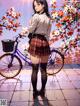 A girl in a school uniform standing next to a bicycle.