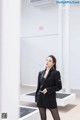 A woman in a black suit standing in a white room.