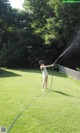 A woman is spraying water on the grass with a hose.