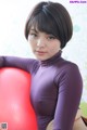 A woman in a purple bodysuit sitting on a red ball.