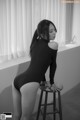 A woman in a black bodysuit sitting on a stool.