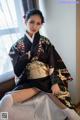 A woman in a black kimono sitting on a bed.