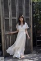 A woman in a white dress standing in front of a wooden door.