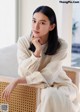 A woman sitting on a wicker chair with her hand on her chin.