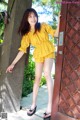 A woman in a yellow top and shorts leaning against a door.