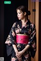 A woman in a black and pink kimono standing in front of a door.