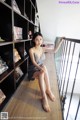 A woman sitting on a wooden floor next to a book shelf.