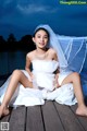 A woman in a wedding dress sitting on a dock.